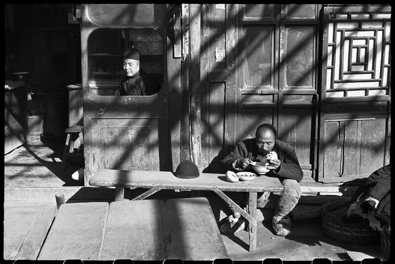 《坐在食肆窗內的跑堂或店主,苦力在簷下用餐,北平,1948年12月》