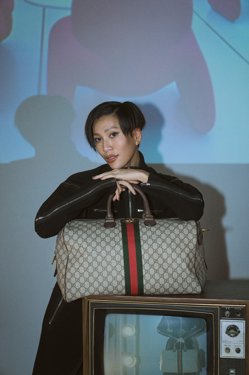 黑色拉鍊洋裝、Gucci Savoy GG 紅綠織帶旅行袋、棕色手提肩背波士頓包,all by Gucci。