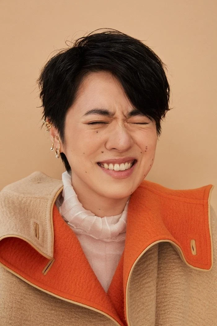 白高領透膚上衣 LOEWE；雙色駱駝斗篷大衣、米色馬褲、小牛皮長靴All by HERMÈS；幾何金耳扣、圓圈線條耳扣、圈形金耳環、字母線條戒指、金色戒指All by APM MONACO。