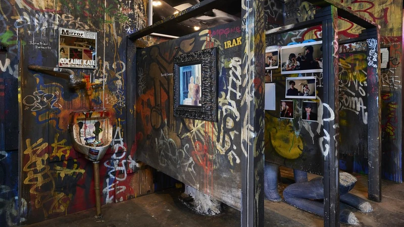 左上角小便斗上的鏡子，是仿造英國《鏡報》報導超模Kate Moss吸食古柯鹼的頭版封面，印有當年標題〈COCAINE KATE〉。