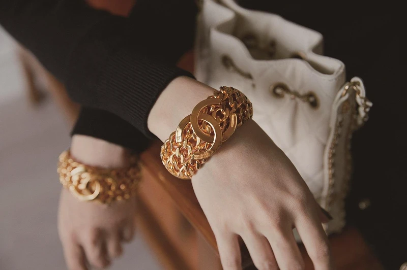 黑白拼接蕾絲緄邊洋裝、黑色十字造型高級樹脂手環、白色菱格紋皮革穿金屬鍊帶水桶包，CHANEL。