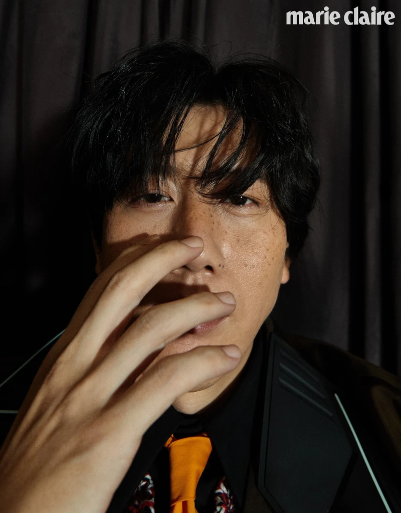 黑色襯衫、明黃領帶、鉤織混紡毛衣、咖啡色尼龍長版風衣、黑長褲、厚底紳士鞋，all by Prada。