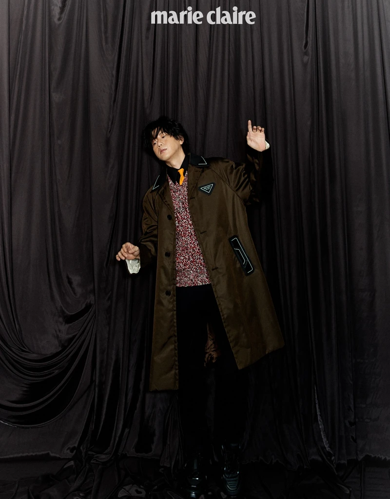 黑色襯衫、明黃領帶、鉤織混紡毛衣、咖啡色尼龍長版風衣、黑長褲、厚底紳士鞋，all by Prada。