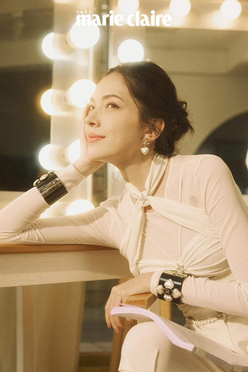 白色真絲縐紗綁帶造型上衣與同款長褲、 雙色皮革短靴、黑色高級樹脂馬爾他十字手環、金屬高級樹脂愛心造型耳環、金屬幻象珍珠腰鍊，all by CHANEL。