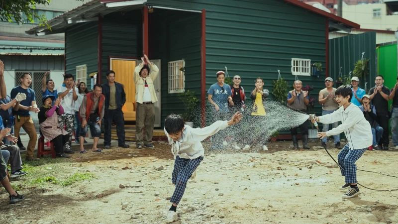 《做工的人 電影版》蓋好新的鐵皮屋之後，眾人在屋外歡樂打水仗，圖為唐浩哲與楊學湧兩位小童星。