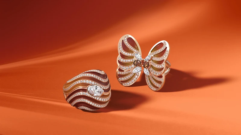 左起：Metamorphosis by De Beers 系列 Autumn 戒指採用三件式套組設計，共可變幻出六種不同佩戴方式，戒指外套部分飾以漸變色大明火琺瑯流線，讓人聯想到盛夏最後一絲餘溫和秋葉的明亮色彩；Autumn蝴蝶造型戒指，以大明火琺瑯巧妙手繪出蝴蝶的翅膀，啡紅色漸層色調以落葉為靈感，與中央橘褐色的鑽石原石呼應。