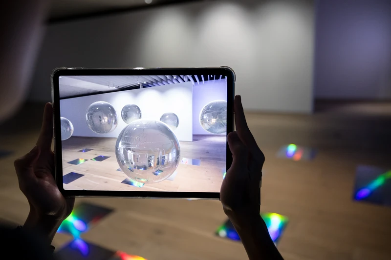 德國藝術家Martin Backes的AR創作〈我知道什麼？我只是個機器？！〉，讓觀眾透過行動裝置與懸浮在美術館空間內的正圓球形機器人相遇、對話 ©忠泰美術館