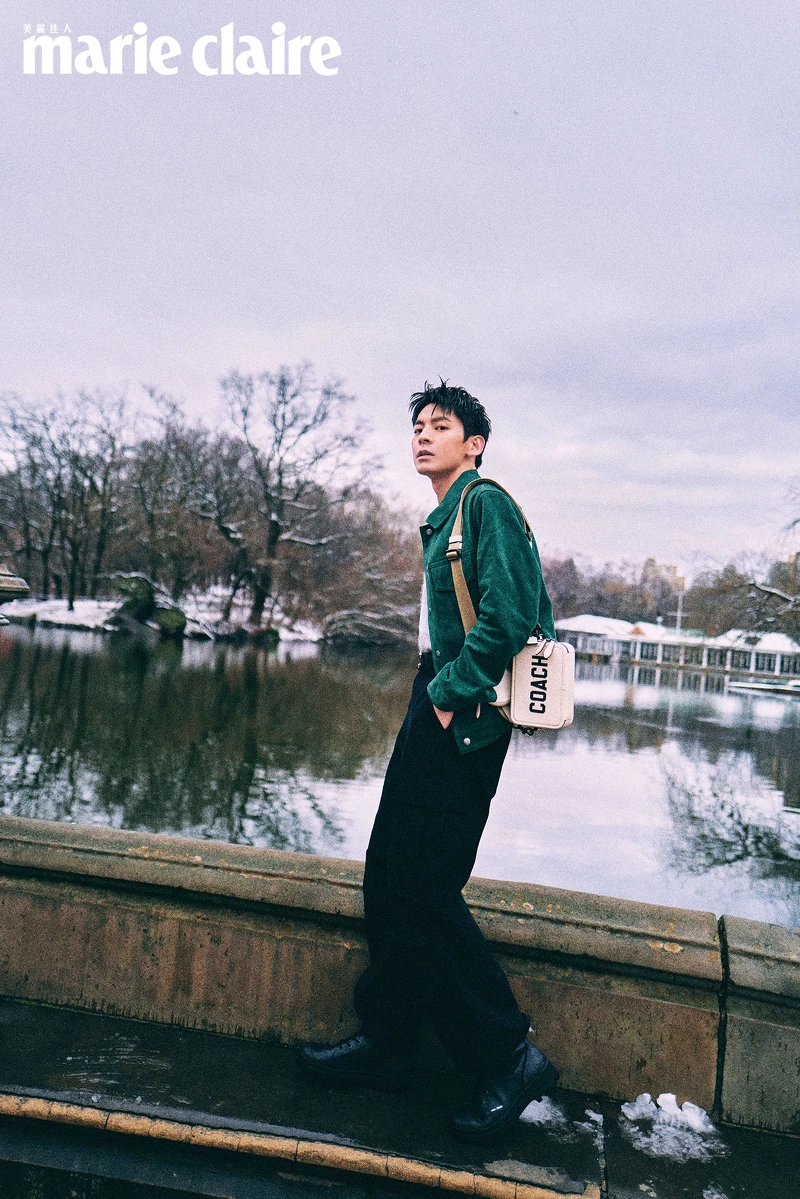 綠色麂皮夾克、藍色條紋背心、黑色寬褲、皮帶、黑色長靴、圖樣斜背手袋，all by Coach。