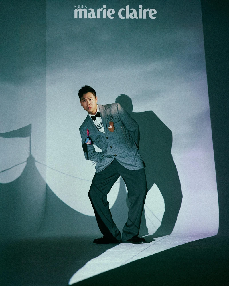 煙灰色工裝直條紋西裝外套、白色 Logo 標語襯衫、煙灰色工裝直條紋西裝褲,All by Moschino;彩色星星領結、黑色皮鞋,Both by Paul Smith。 煙灰色工裝直條紋西裝外套、白色 Logo 標語襯衫、煙灰色工裝直條紋西裝褲,All by Moschino;彩色星星領結、黑色皮鞋,Both by Paul Smith。