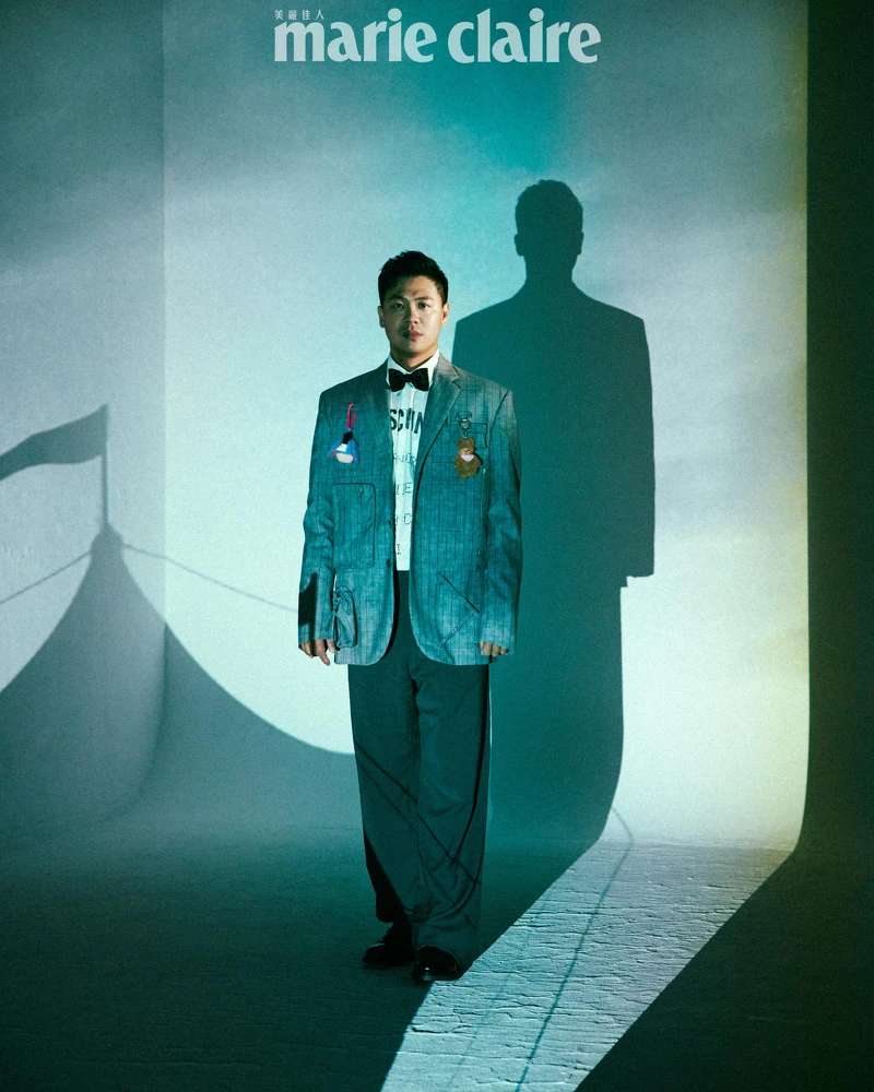 煙灰色工裝直條紋西裝外套、白色 Logo 標語襯衫、煙灰色工裝直條紋西裝褲,All by Moschino;彩色星星領結、黑色皮鞋,Both by Paul Smith。 煙灰色工裝直條紋西裝外套、白色 Logo 標語襯衫、煙灰色工裝直條紋西裝褲,All by Moschino;彩色星星領結、黑色皮鞋,Both by Paul Smith。