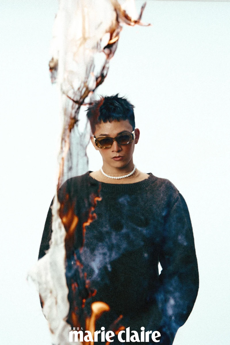 橘色短袖上衣、灰棕色毛衣，both by Prada；黑色西裝褲、琥珀色墨鏡 both by Loewe；琥珀色墨鏡，Loewe。